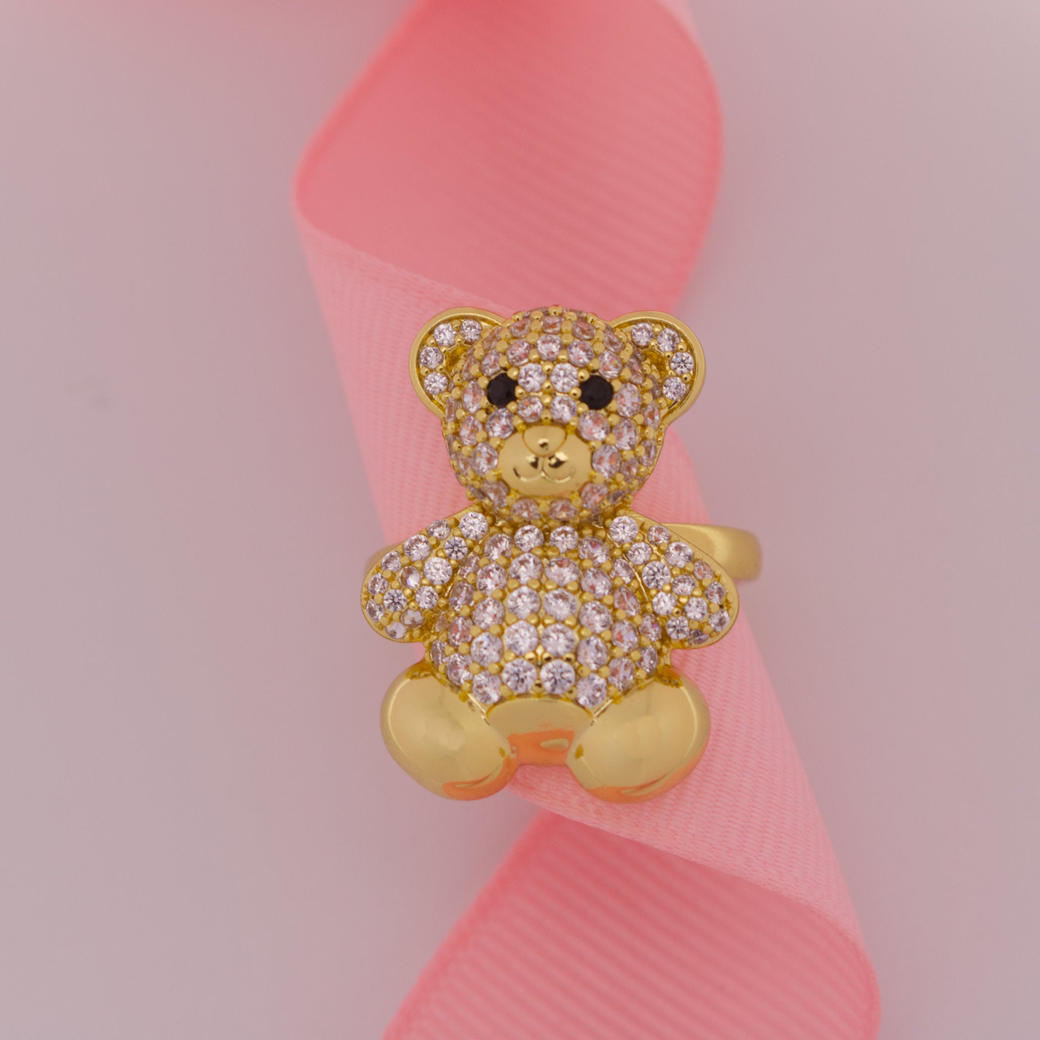 Gold teddy bear-shaped ring with gemstones on a pink ribbon