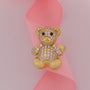 Gold teddy bear-shaped ring with gemstones on a pink ribbon
