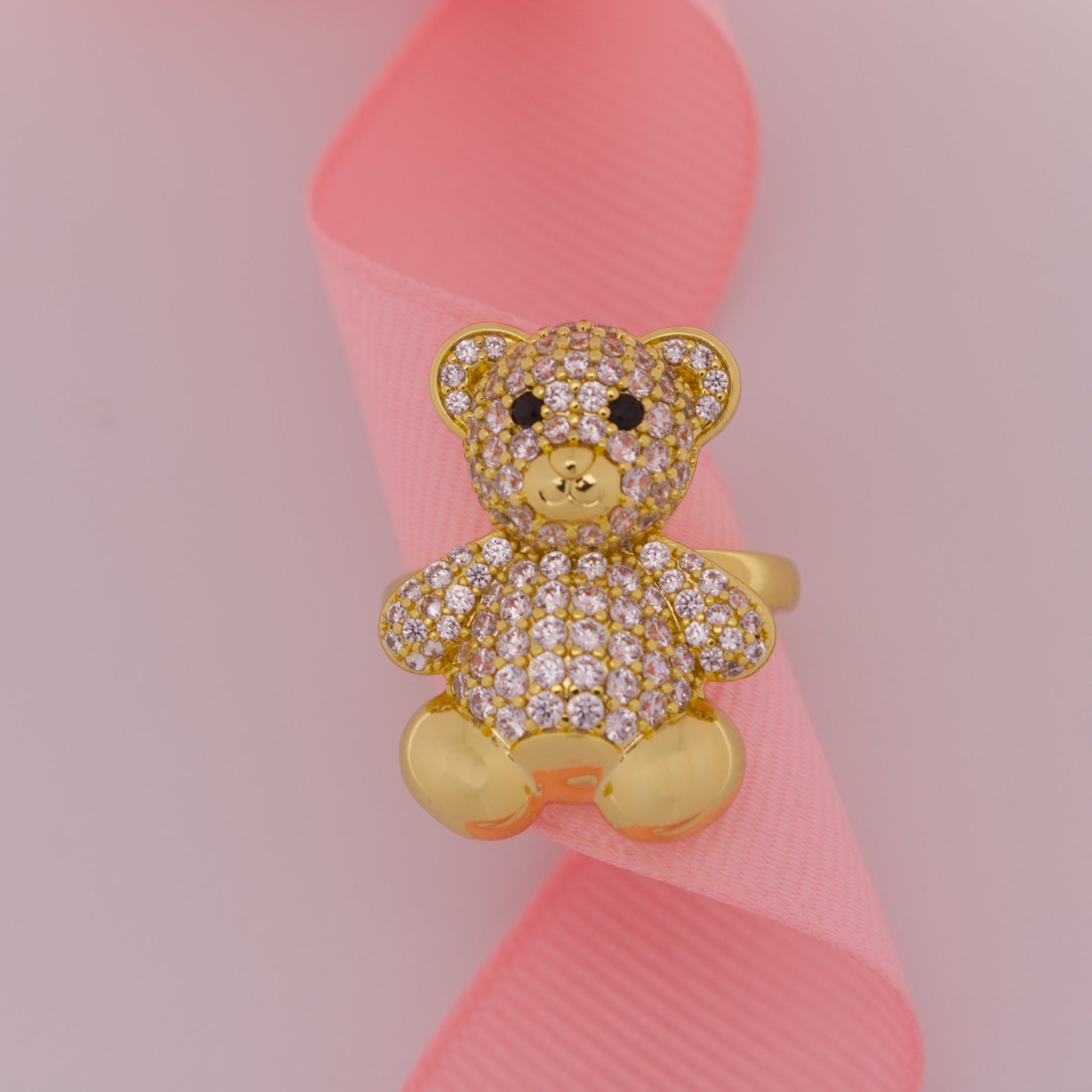 Gold teddy bear-shaped ring with gemstones on a pink ribbon