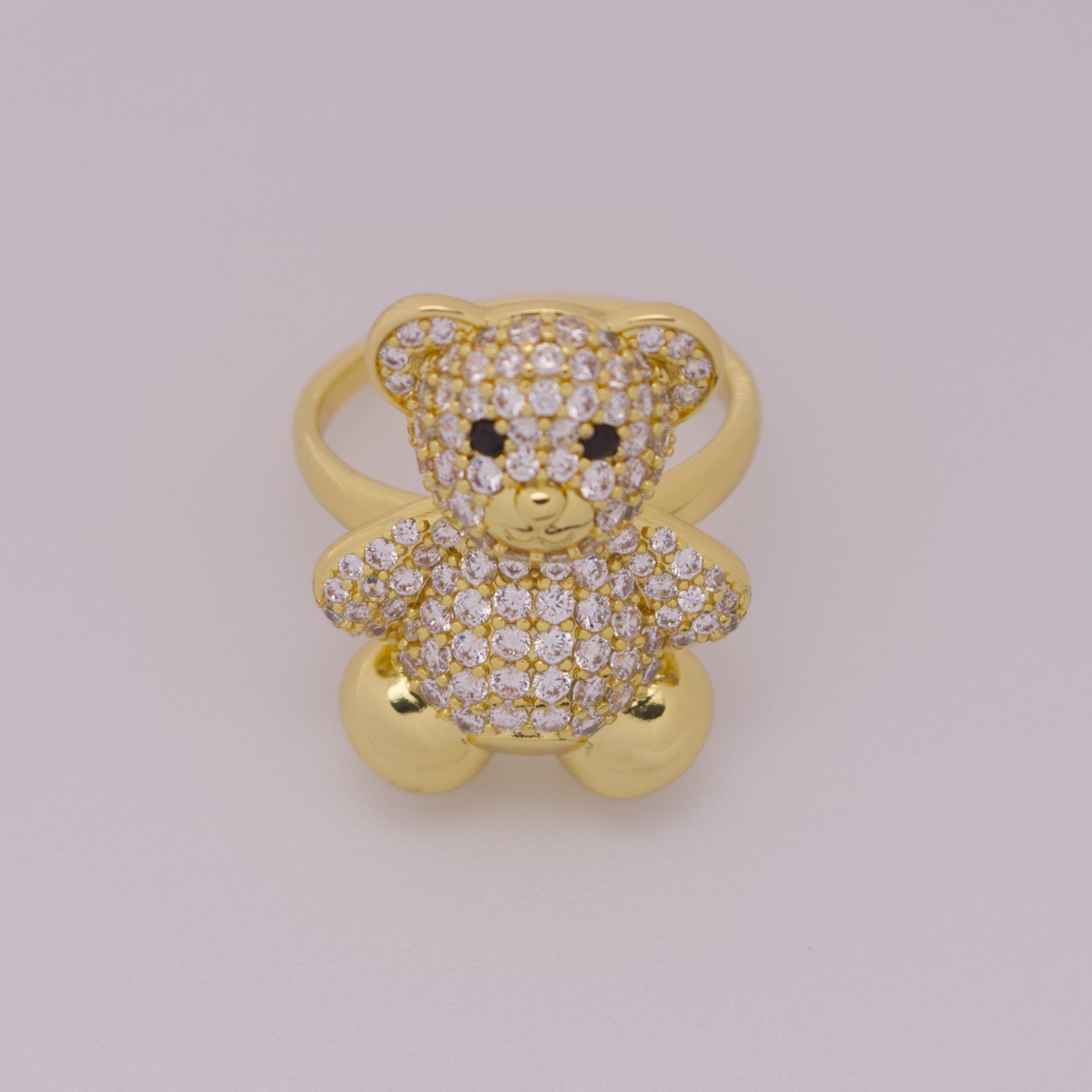 Gold teddy bear-shaped ring with gemstones on a light gray background