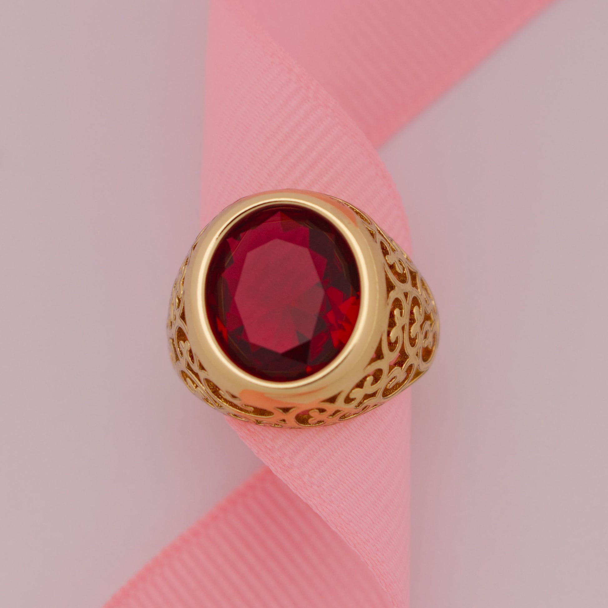 Gold ring with a red gemstone on a pink ribbon