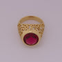 Gold ring with a red gemstone on a light gray background
