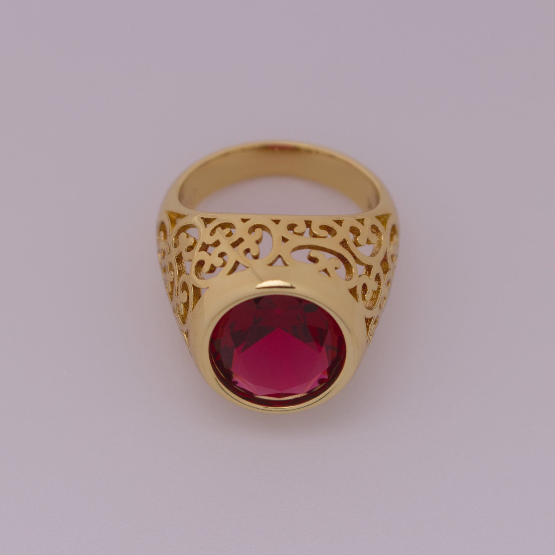Gold ring with a red gemstone on a light gray background