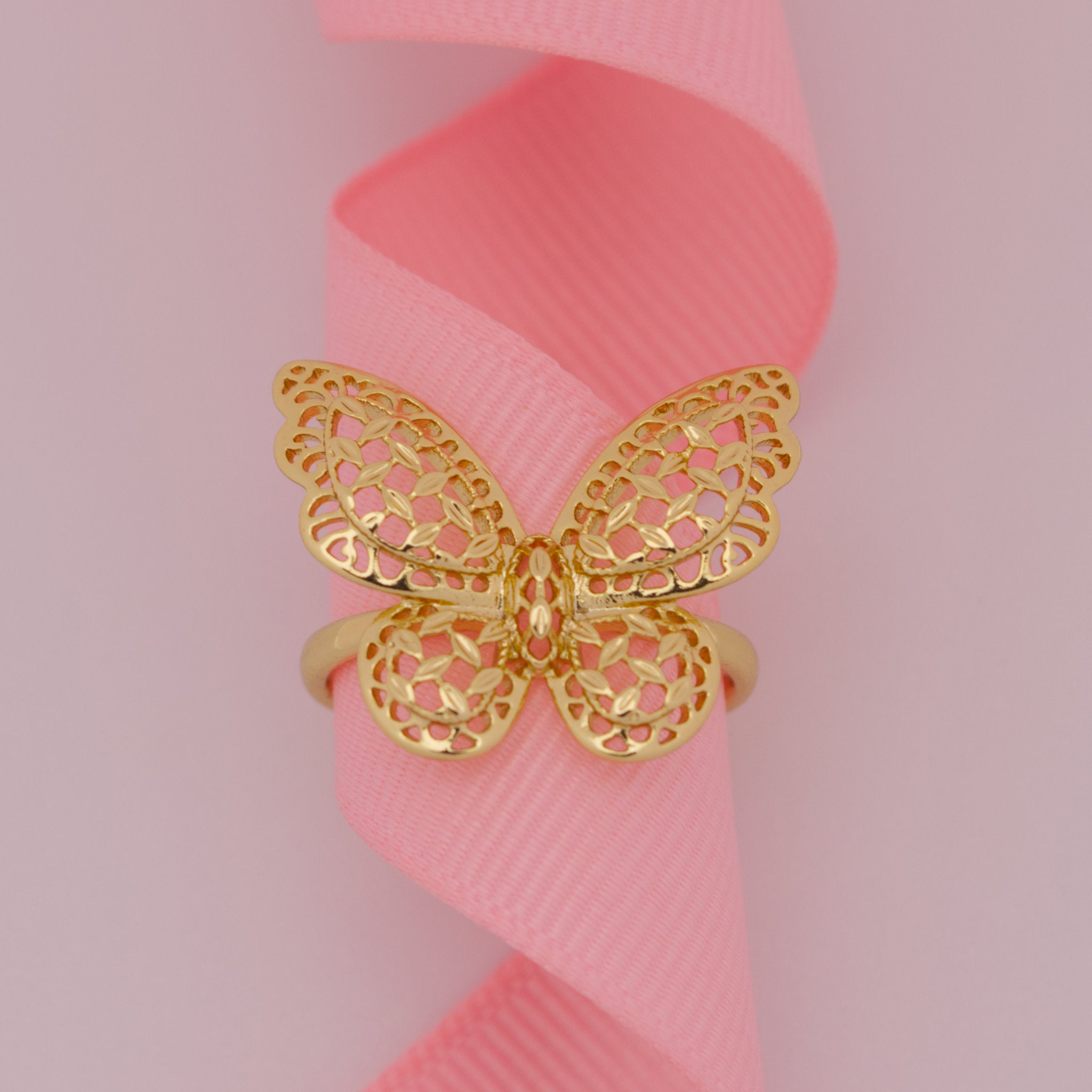 Gold butterfly ring on a pink ribbon with a pink background