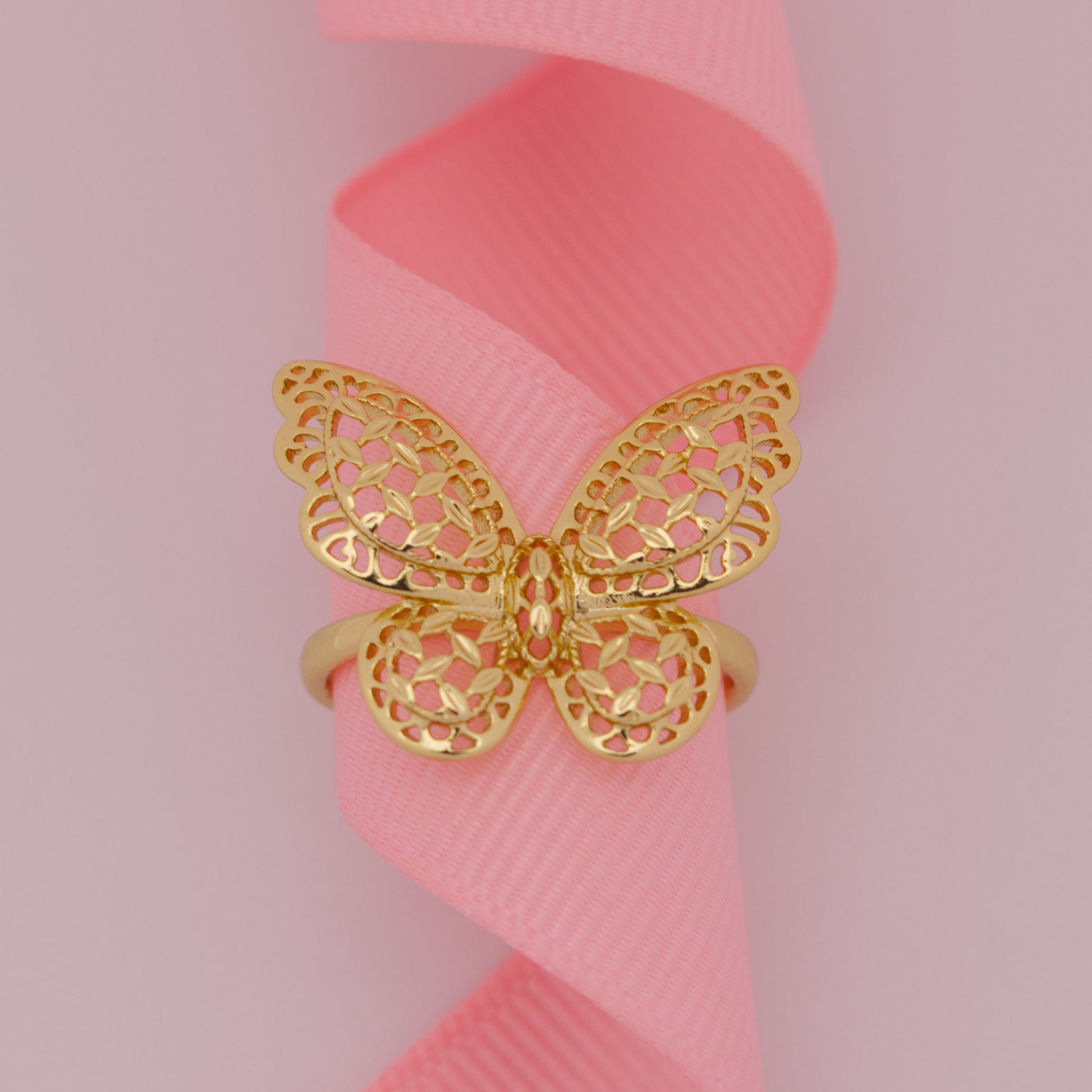 Gold butterfly ring on a pink ribbon with a pink background
