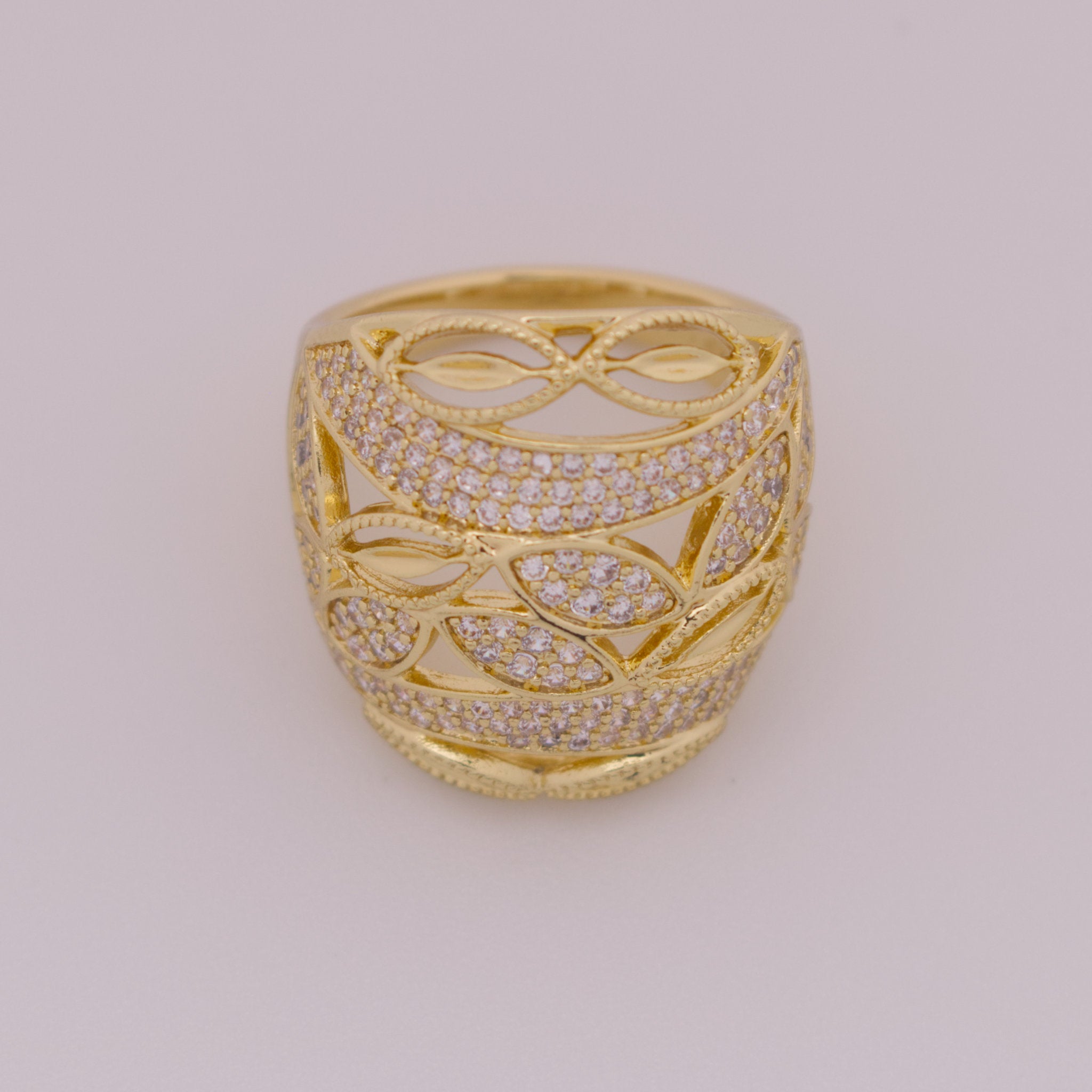 Gold ring with intricate design and diamond accents on a light gray background