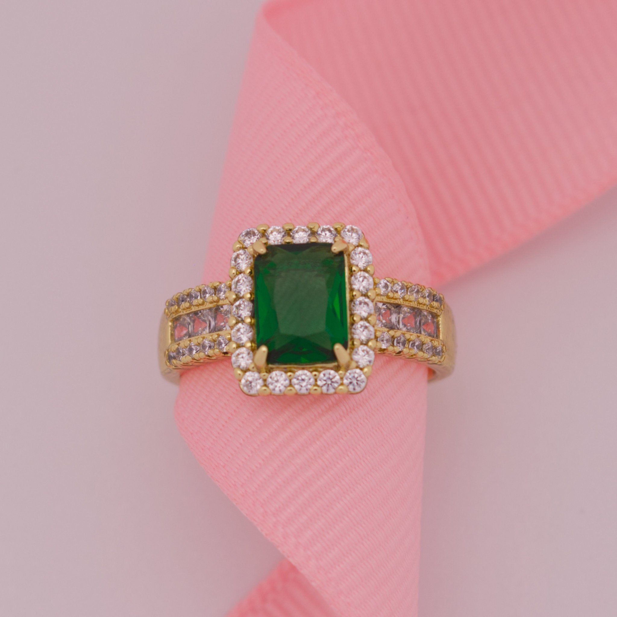 Gold ring with a green gemstone on a pink ribbon