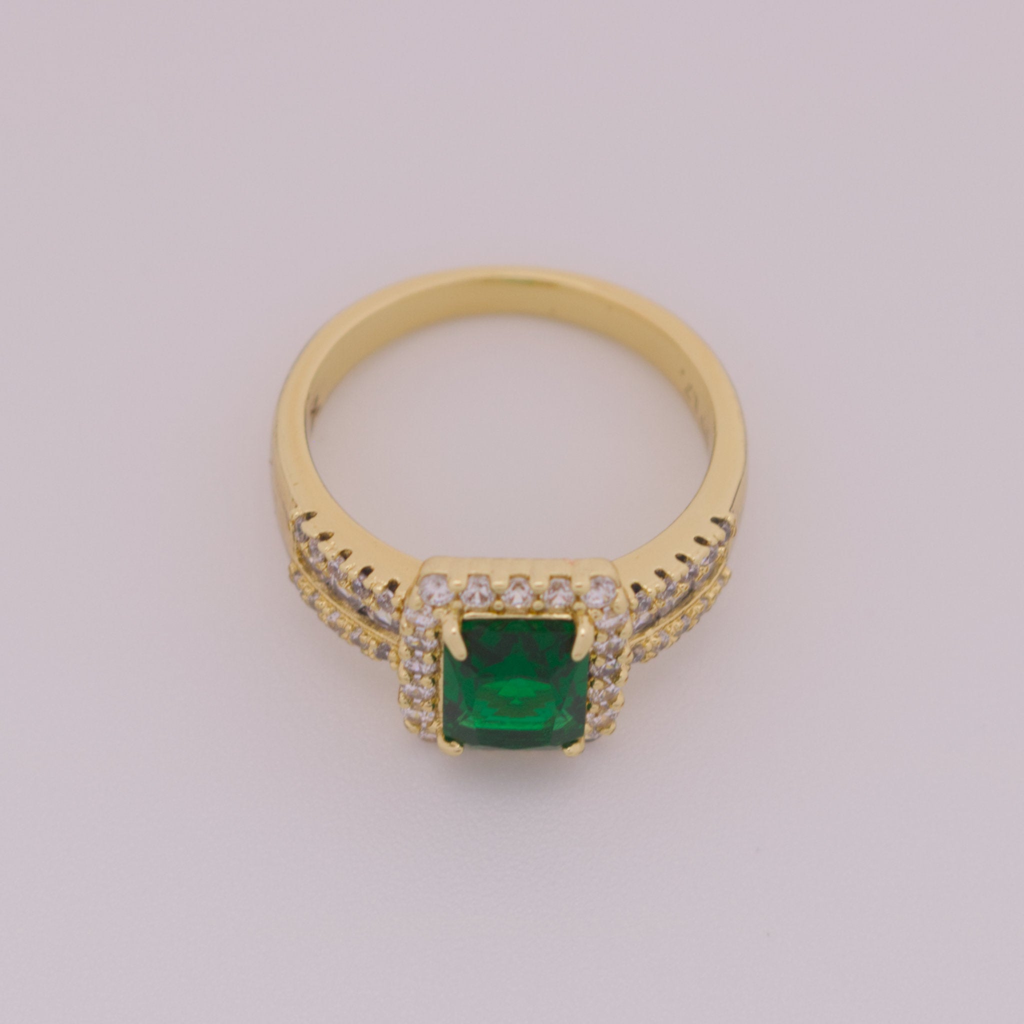 Gold ring with a green gemstone on a light gray background