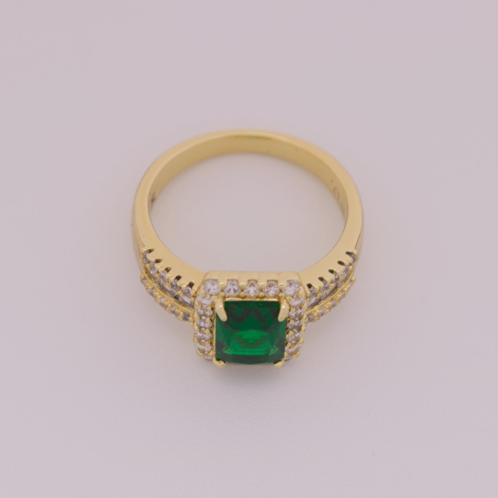 Gold ring with a green gemstone on a light gray background