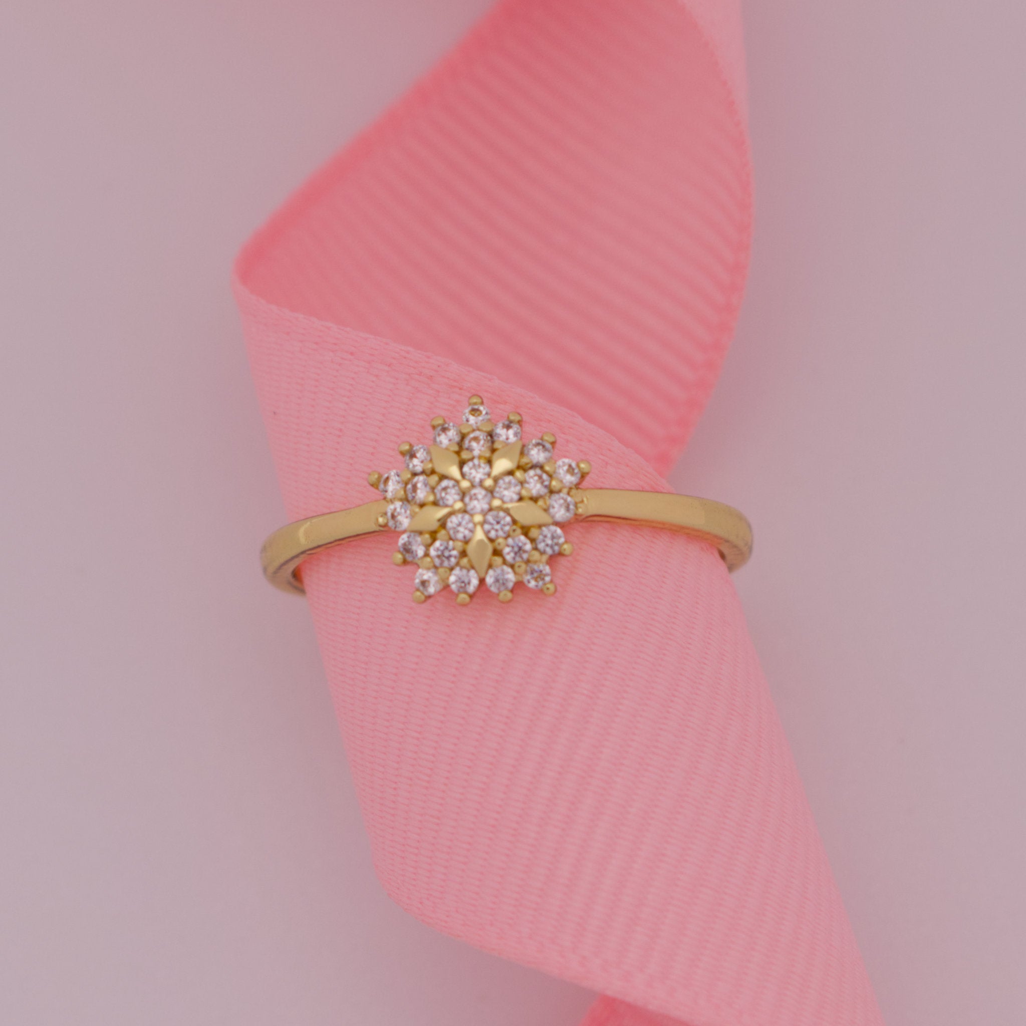 Gold ring with a diamond-like center on a pink ribbon