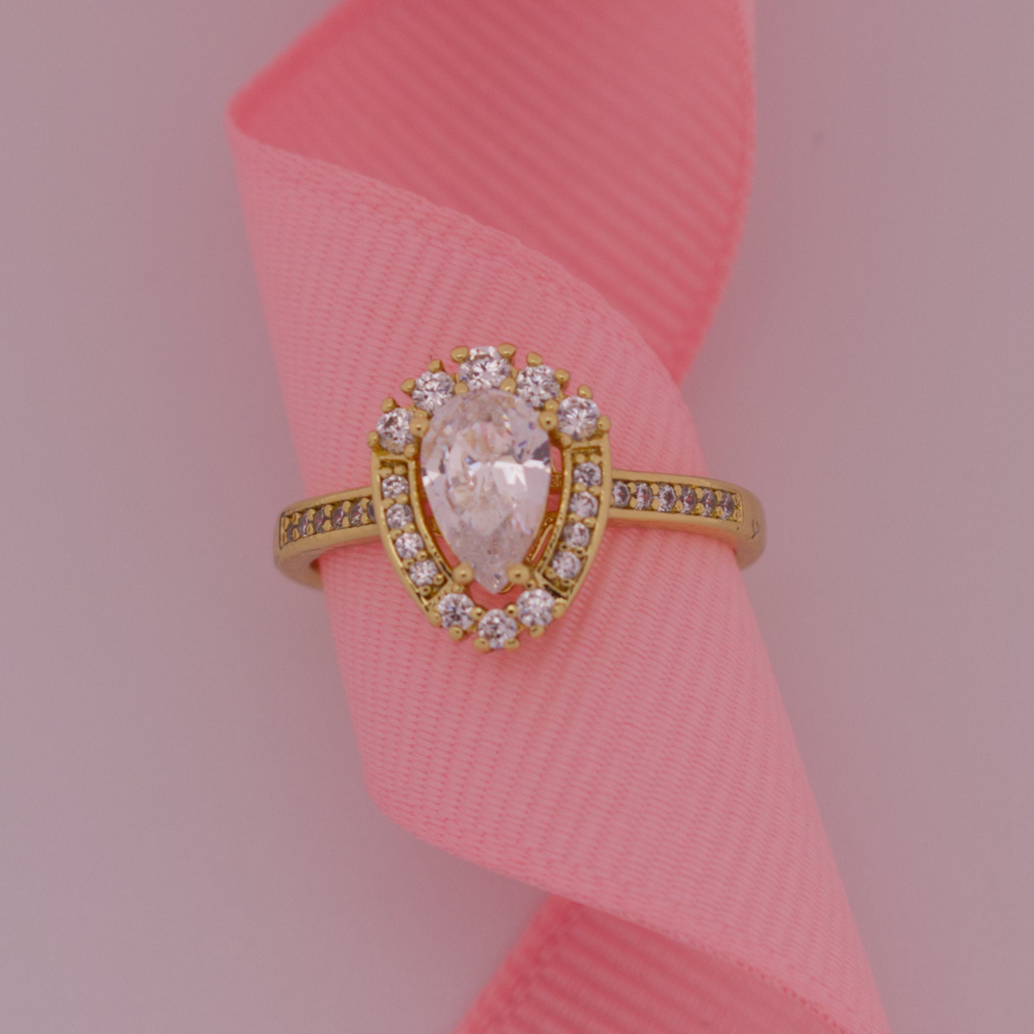 Gold ring with a large central gemstone and smaller stones on a pink ribbon background