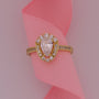 Gold ring with a large central gemstone and smaller stones on a pink ribbon background