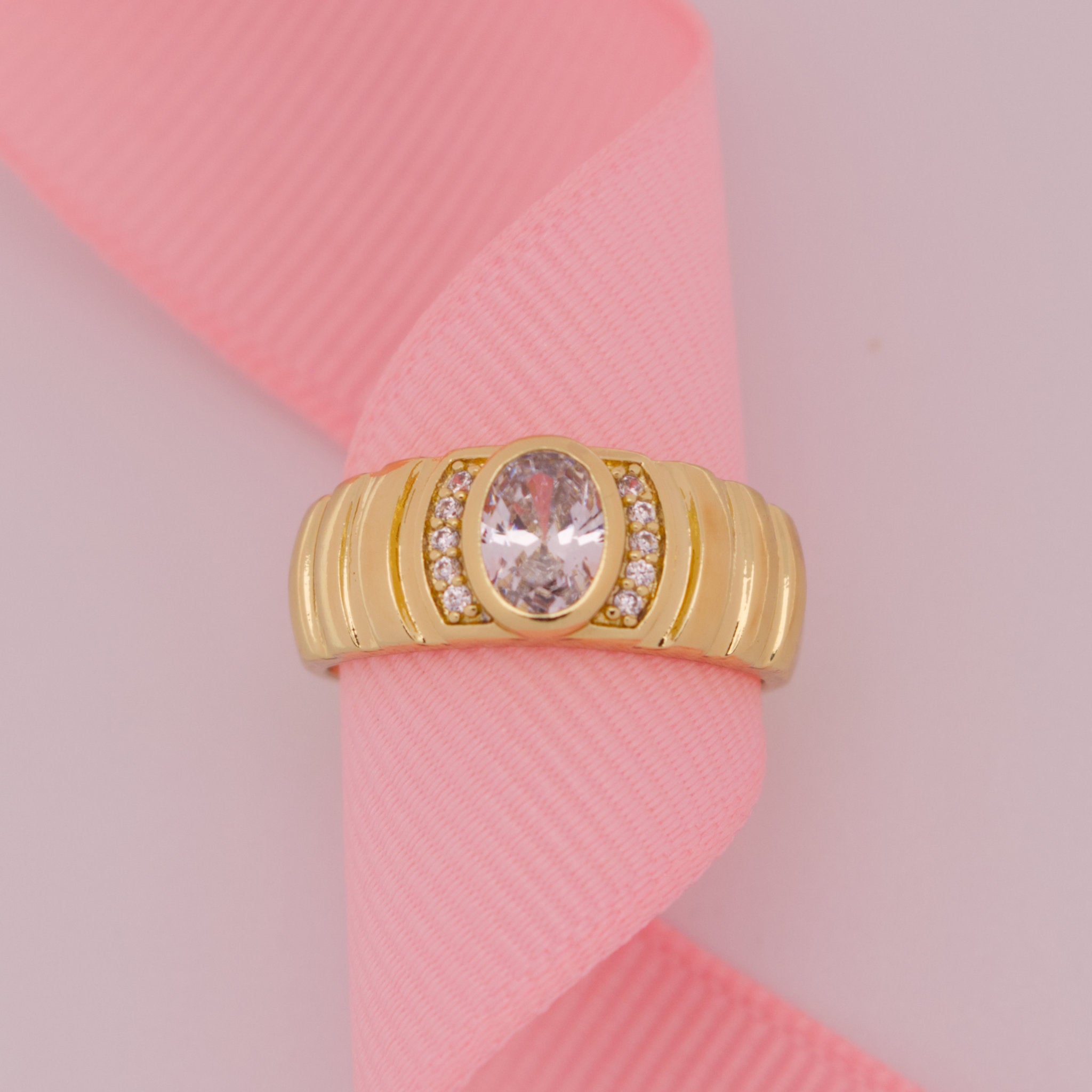 Gold ring with a large central gemstone on a pink ribbon