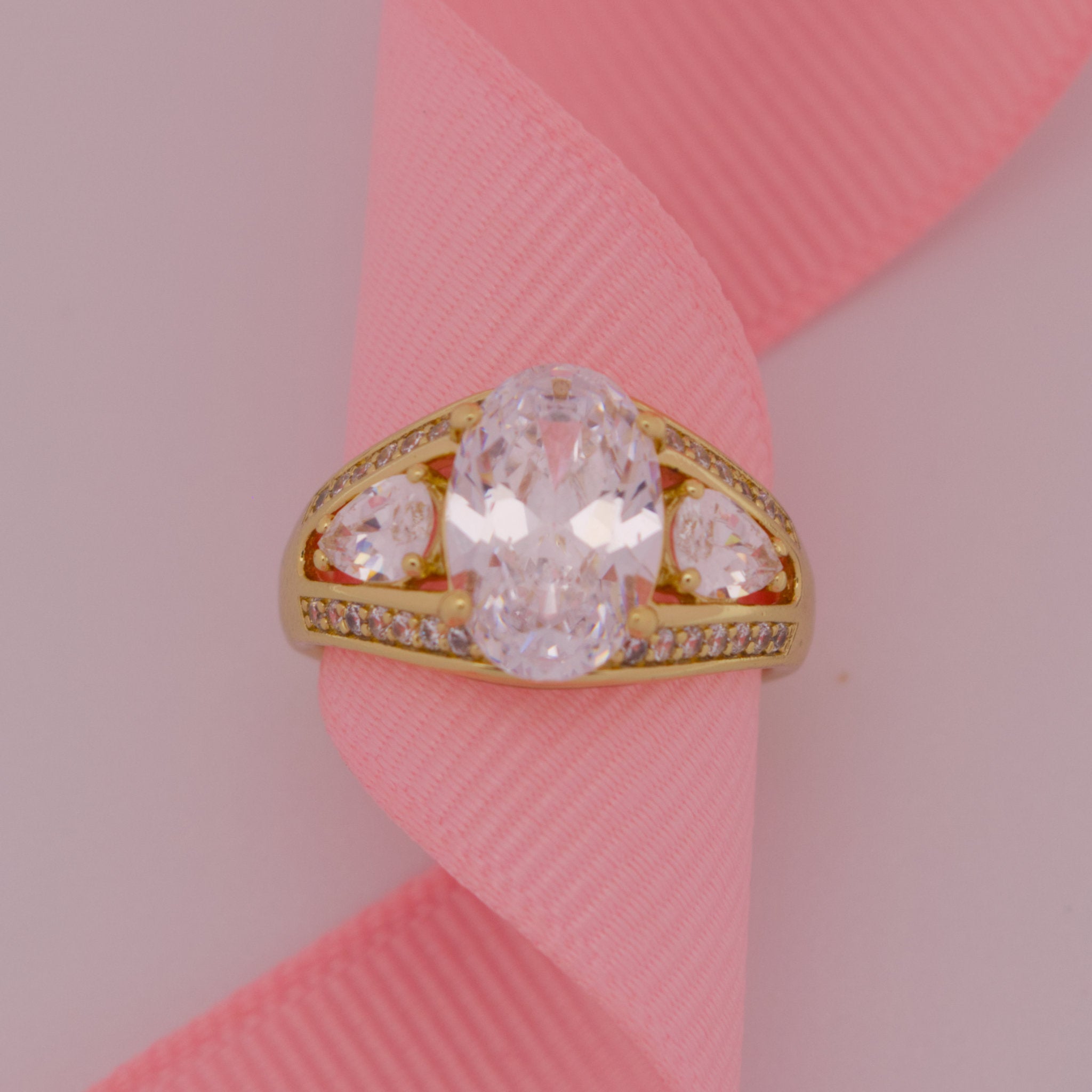 Gold ring with a large central diamond and smaller diamonds on a pink ribbon background