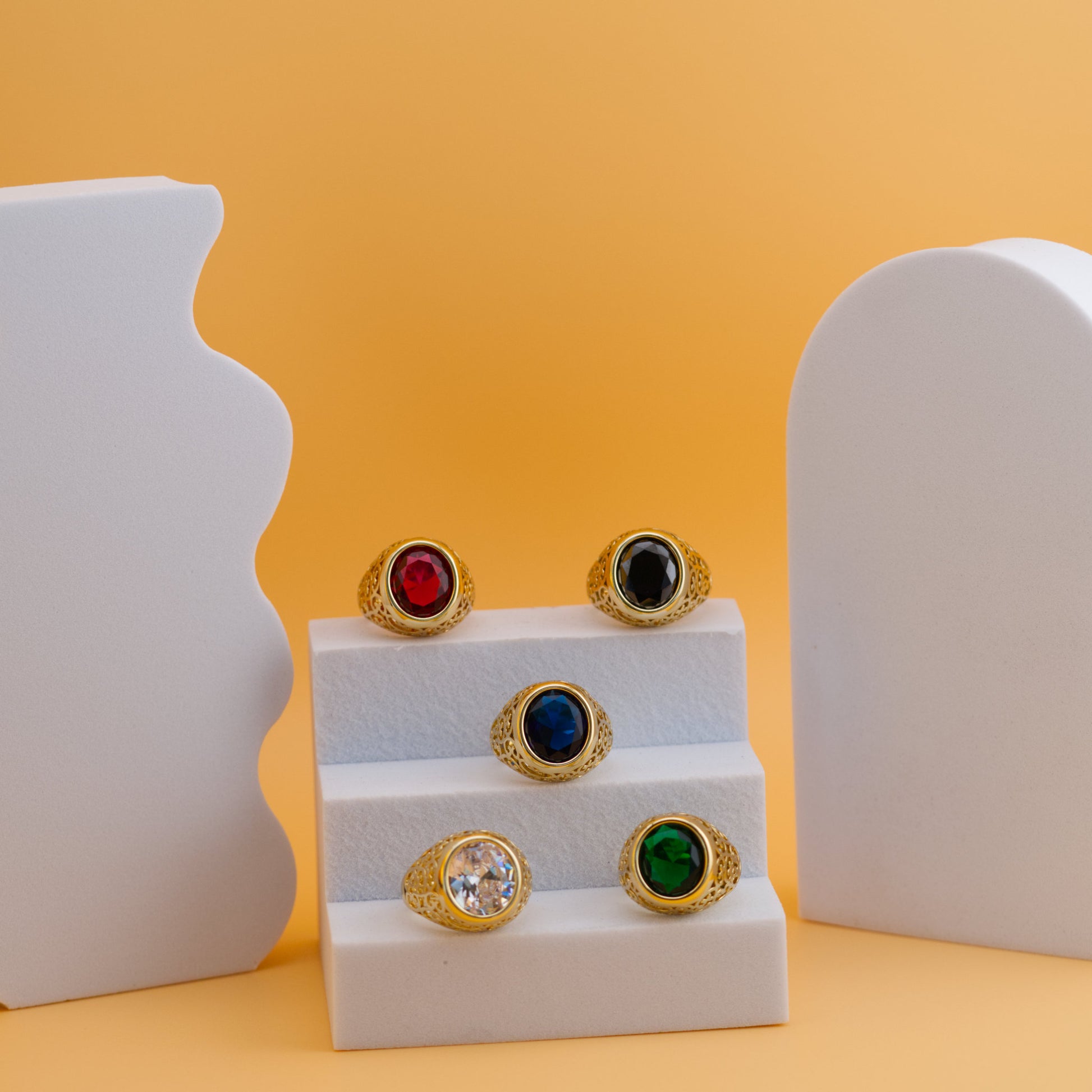 Set of gold earrings with colored stones on a white stand against an orange background