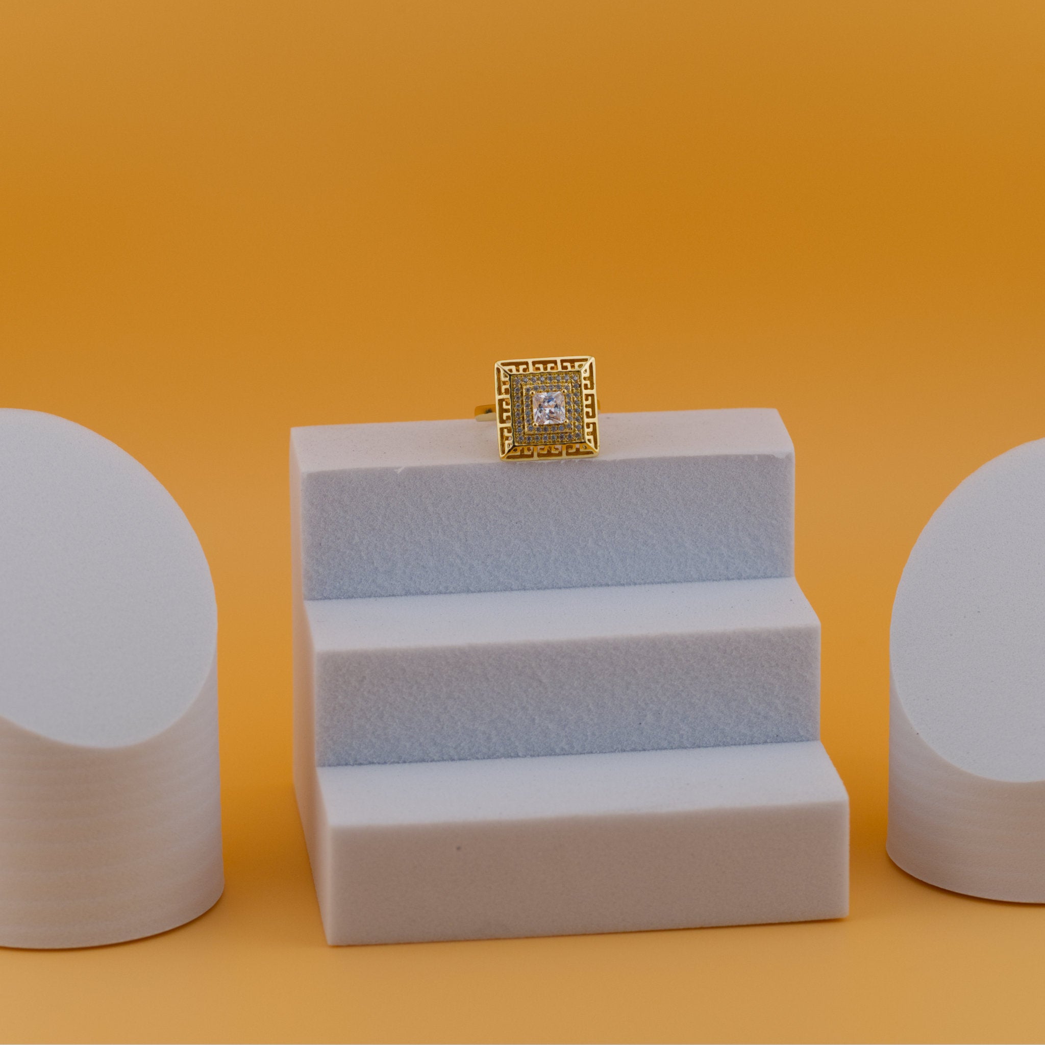 Gold ring with a diamond on a white stand against an orange background