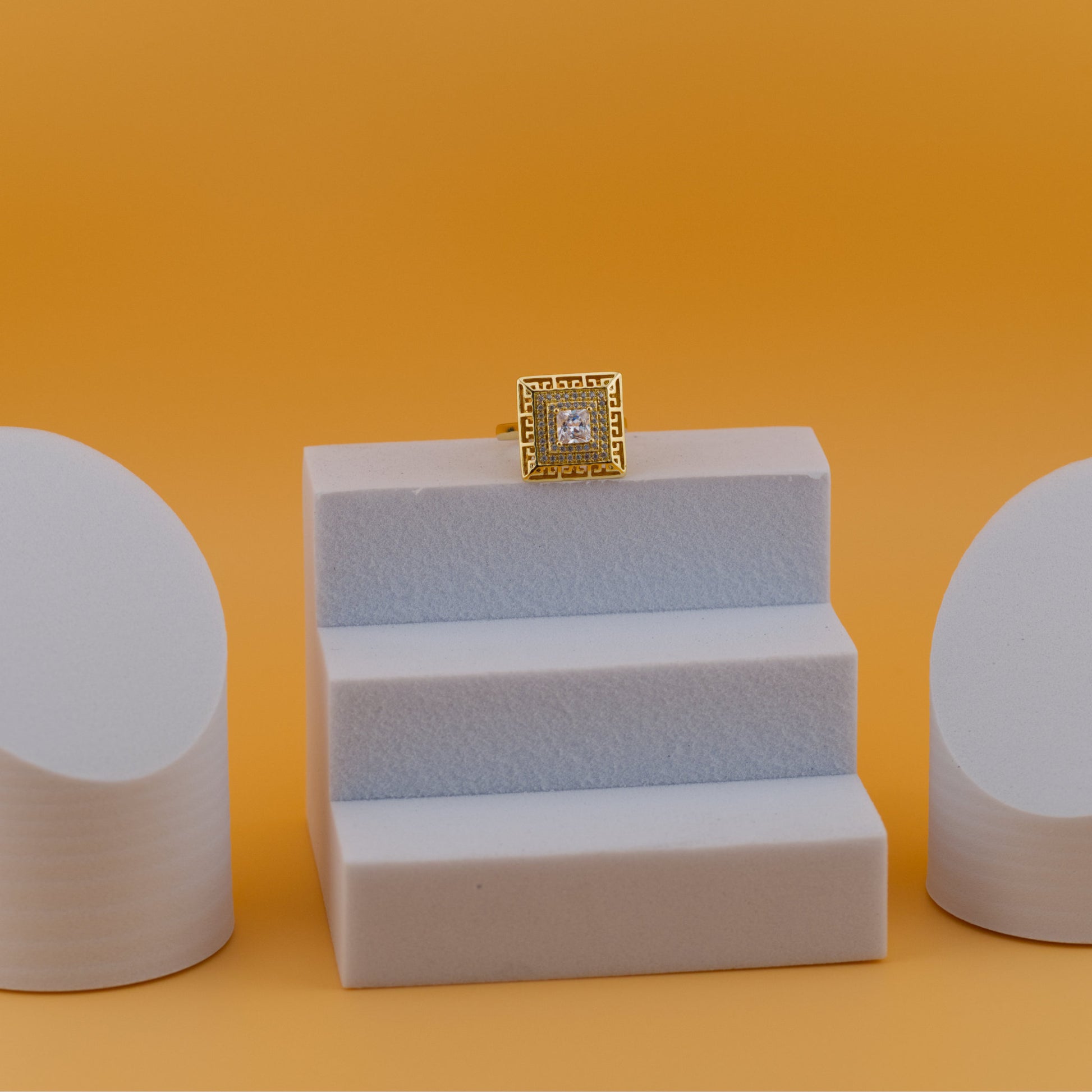 Gold ring with a diamond on a white stand against an orange background