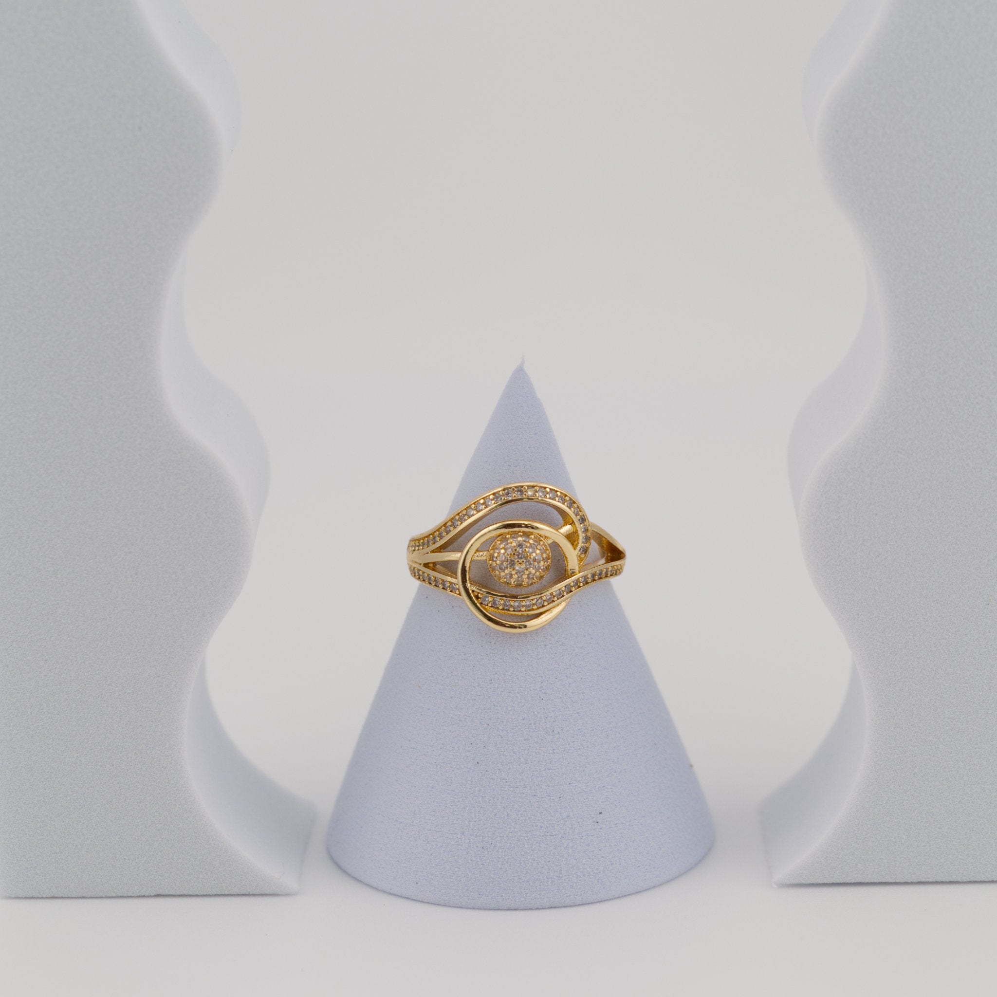 Gold ring on a gray cone-shaped stand against a light gray background