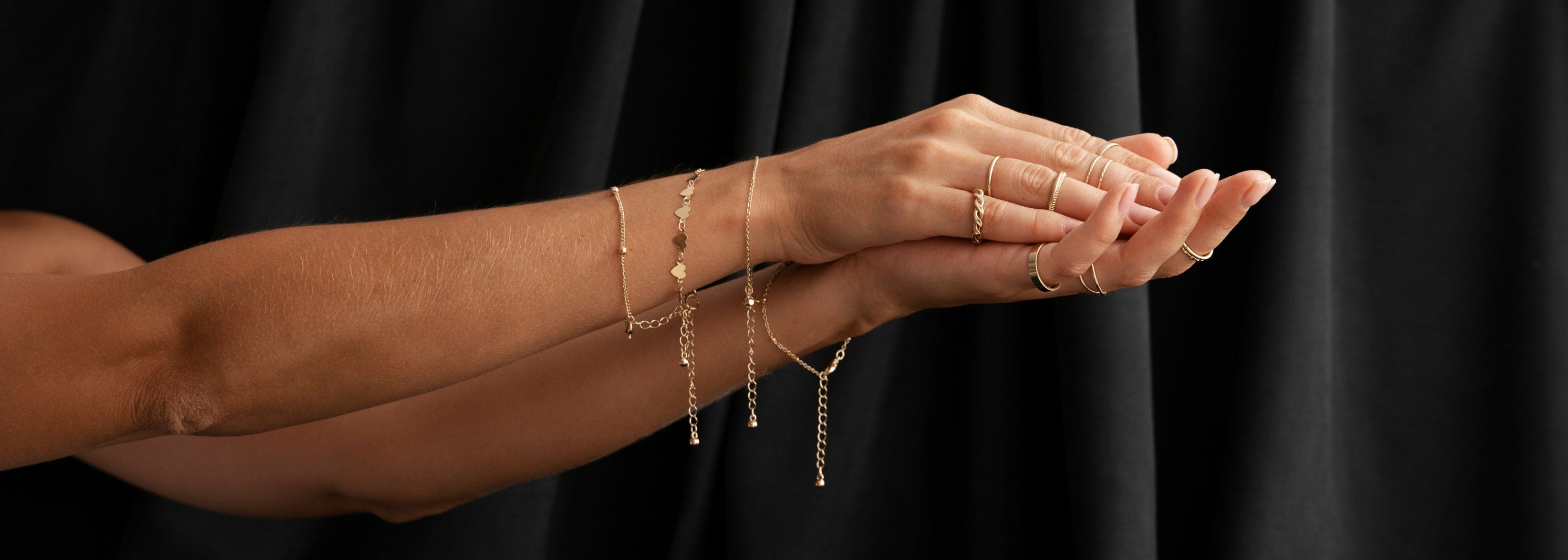 Hands wearing gold jewelry against a black background