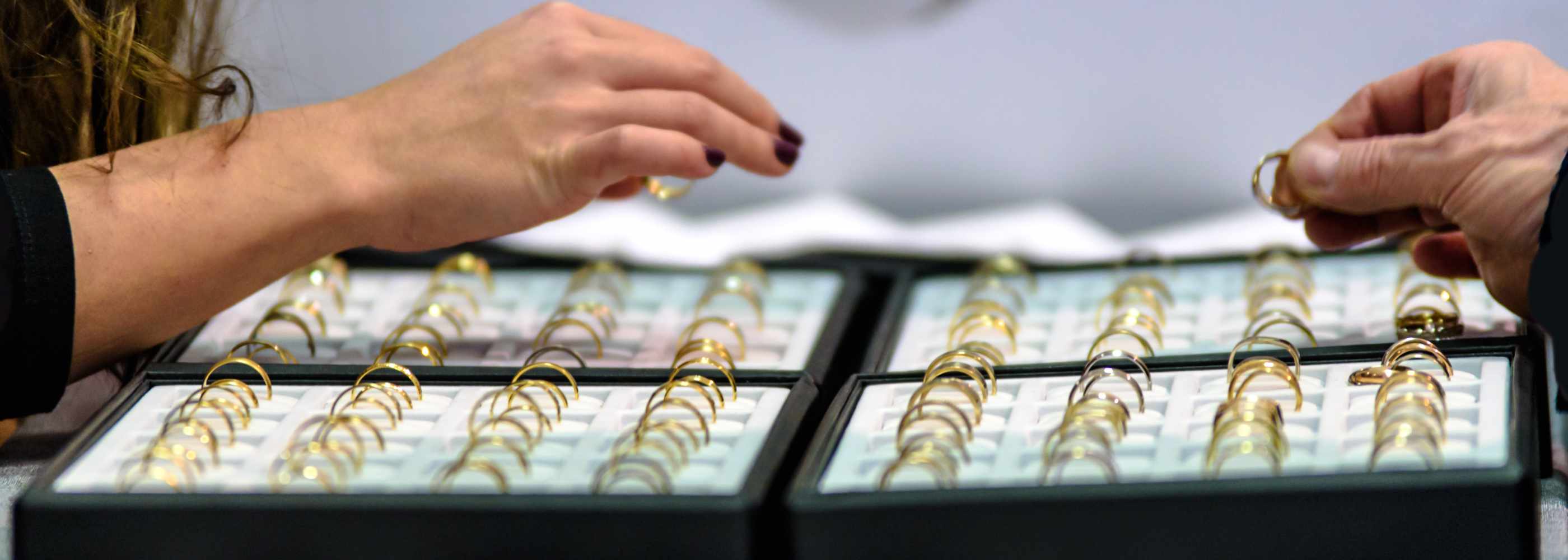 Two people examining gold rings in a display case.