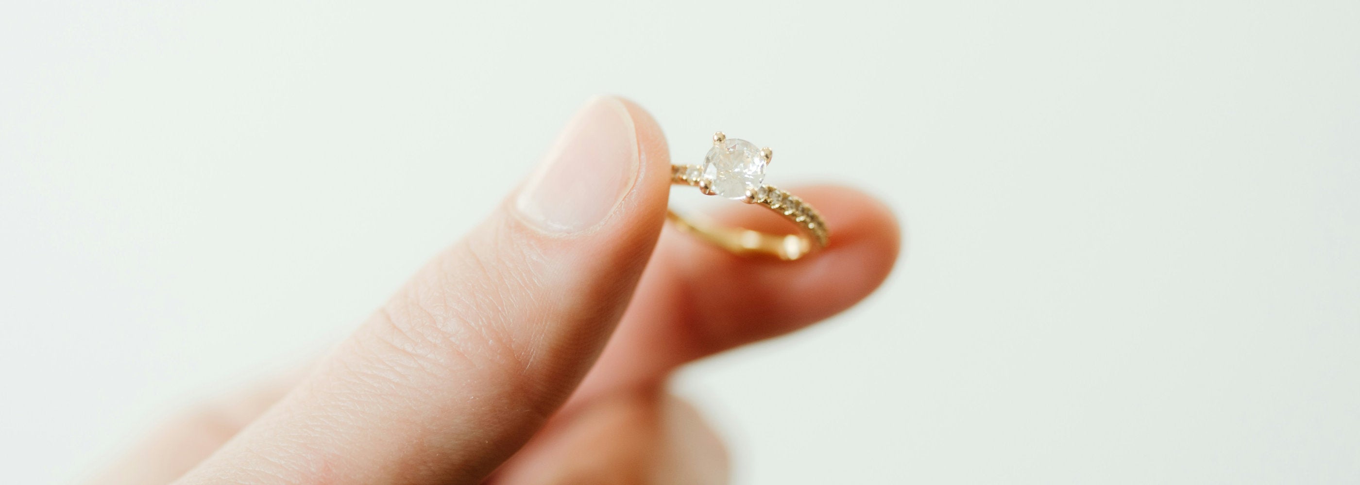 Gold ring with a stone on a finger against a white background