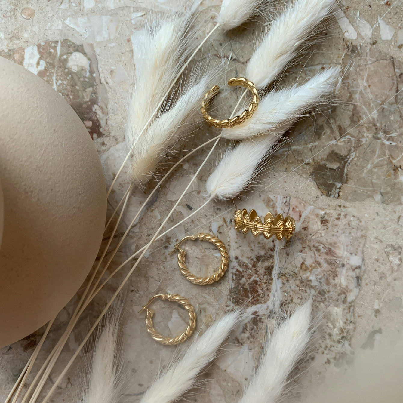 Gold hoop earrings on a textured surface with dried grasses and feathers