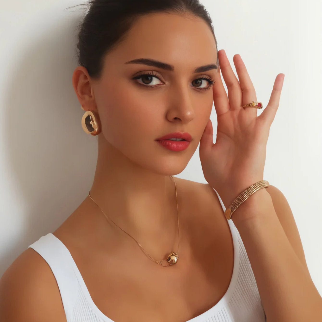 Woman wearing gold jewelry including earrings, necklace, bracelet, and ring against a plain background