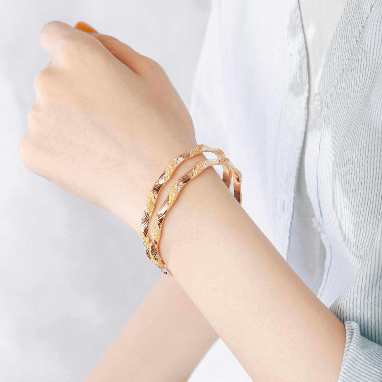 Hand wearing a gold bracelet on a light background