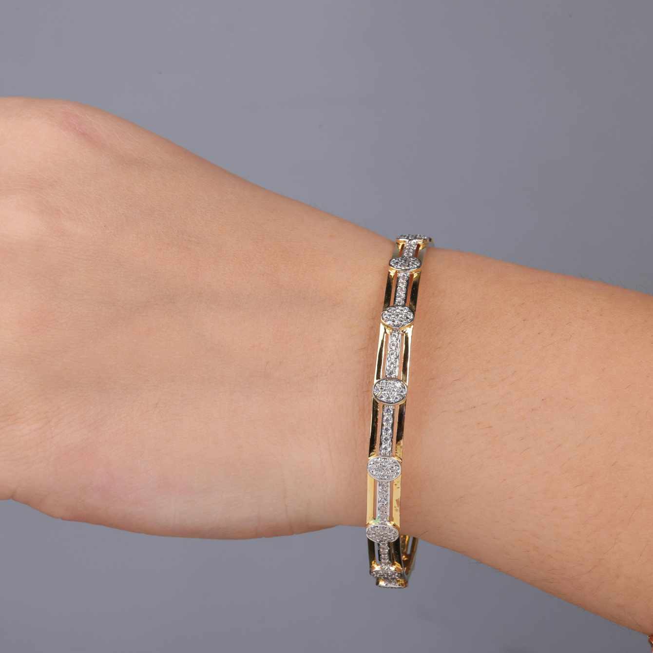 Gold bracelet with diamonds on a wrist against a gray background