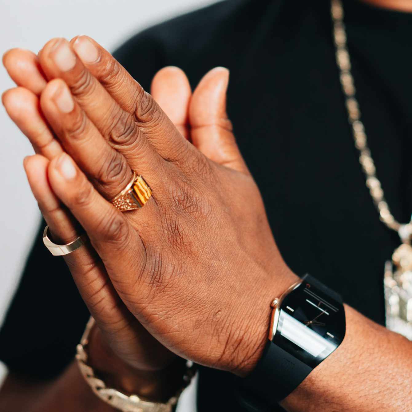 Close-up of hands with a gold ring and black watch, wearing a gold bracelet.